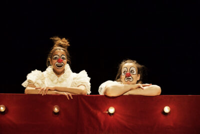 Kuvassa kaksi klovnia kurkistaa verhon yli.